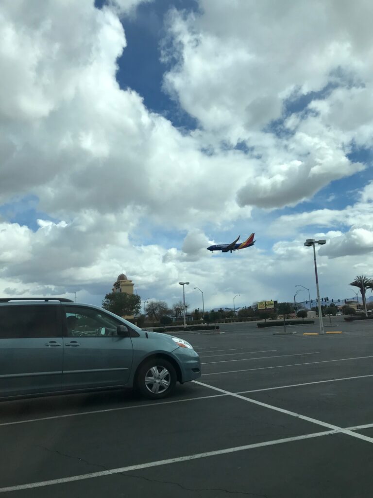 Southwest Airlines plane landing over a parking lot with a blue minivan. Cloudy sky.
