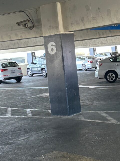 Parking garage pillar with the number 6, surrounded by parked cars.